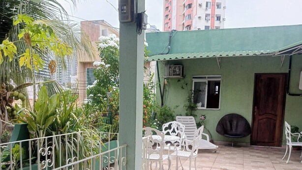 Eine überdachte Terrasse im Freien mit Fliesenboden, weißen Metallgeländern und verschiedenen topfpflanzen.