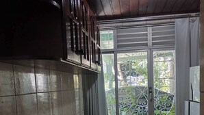 Eine Küche mit gefliestem Fliesenspiegel, einem Holztisch und Stühlen. Es gibt ein Fenster mit Metallgitter und Blick auf Grünfläche.