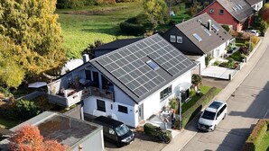 A residential house with a solar panel roof, a garage, and a driveway with a parked car.