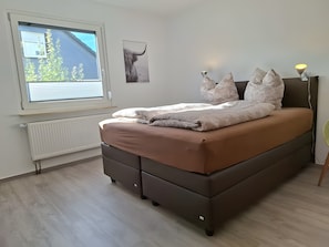 A bedroom with a bed, a radiator, a window, and a wall-mounted lamp.