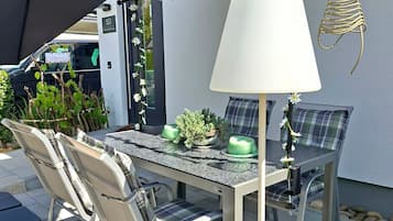 Een terras buiten met een tafel en stoelen, een lamp en een decoratieve plantencompositie.