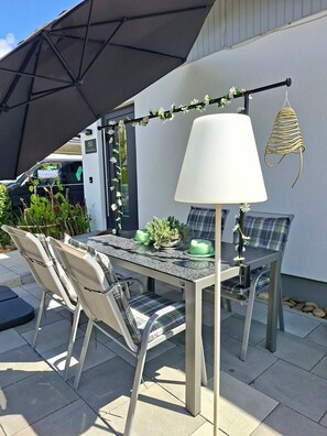 An outdoor patio with a table and chairs, a lamp, and a decorative plant arrangement.