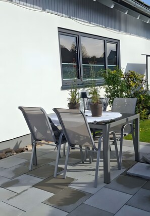 A modern outdoor patio with a table and chairs, a potted plant, and a window.