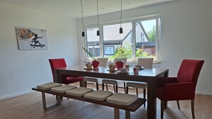 A dining area with a wooden table, red chairs, a bench, and a window with a view of houses.