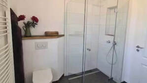 Een moderne badkamer met een glazen douchecabine, een wit toilet en een klein houten plankje met een bloevas.