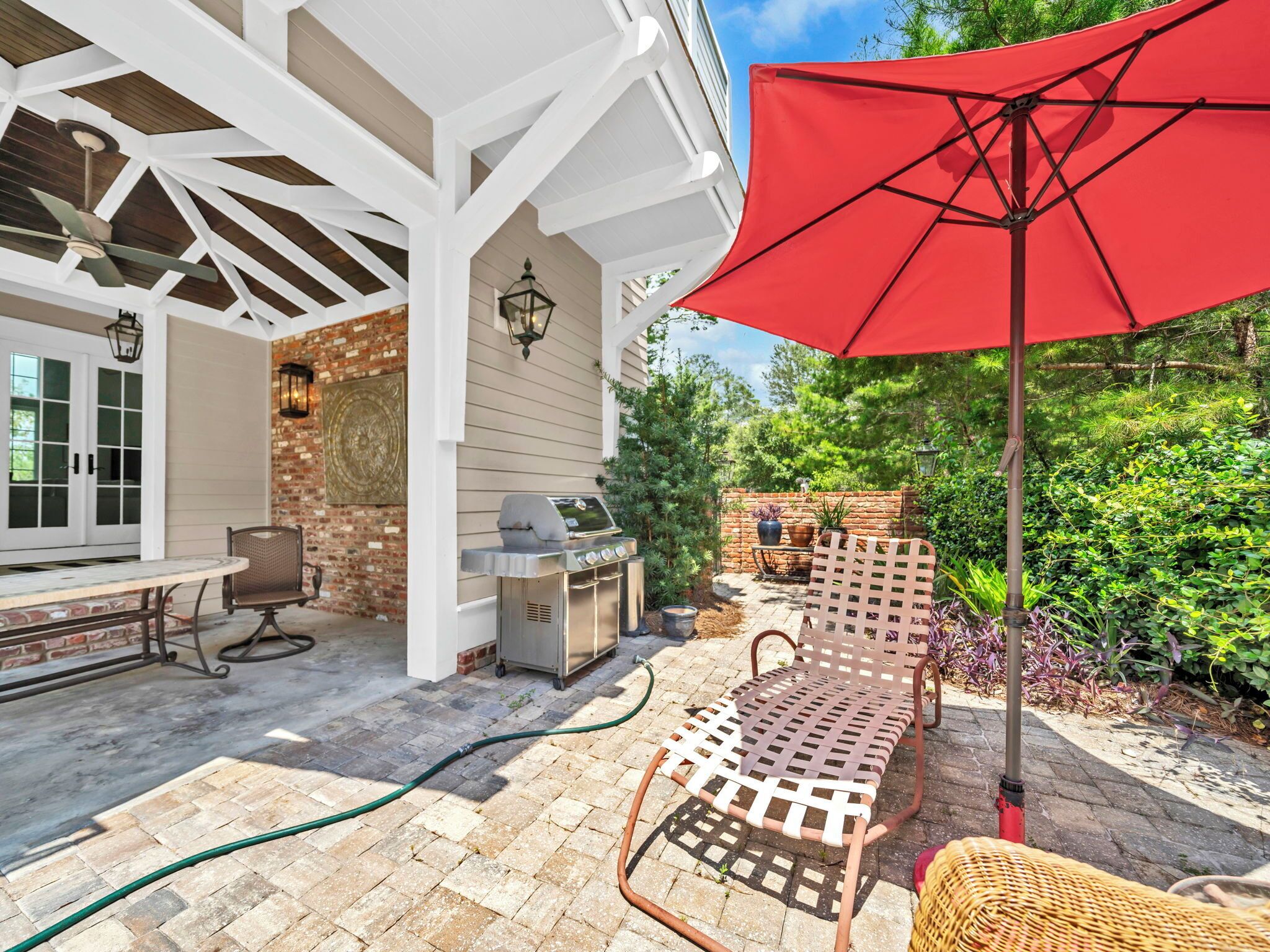 Une terrasse extérieure avec un barbecue, un parasol rouge et un coin salon avec une chaise en osier.