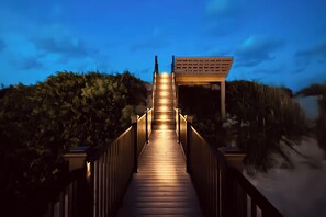 A wooden staircase leading to a covered area with a view of the beach and vegetation.
