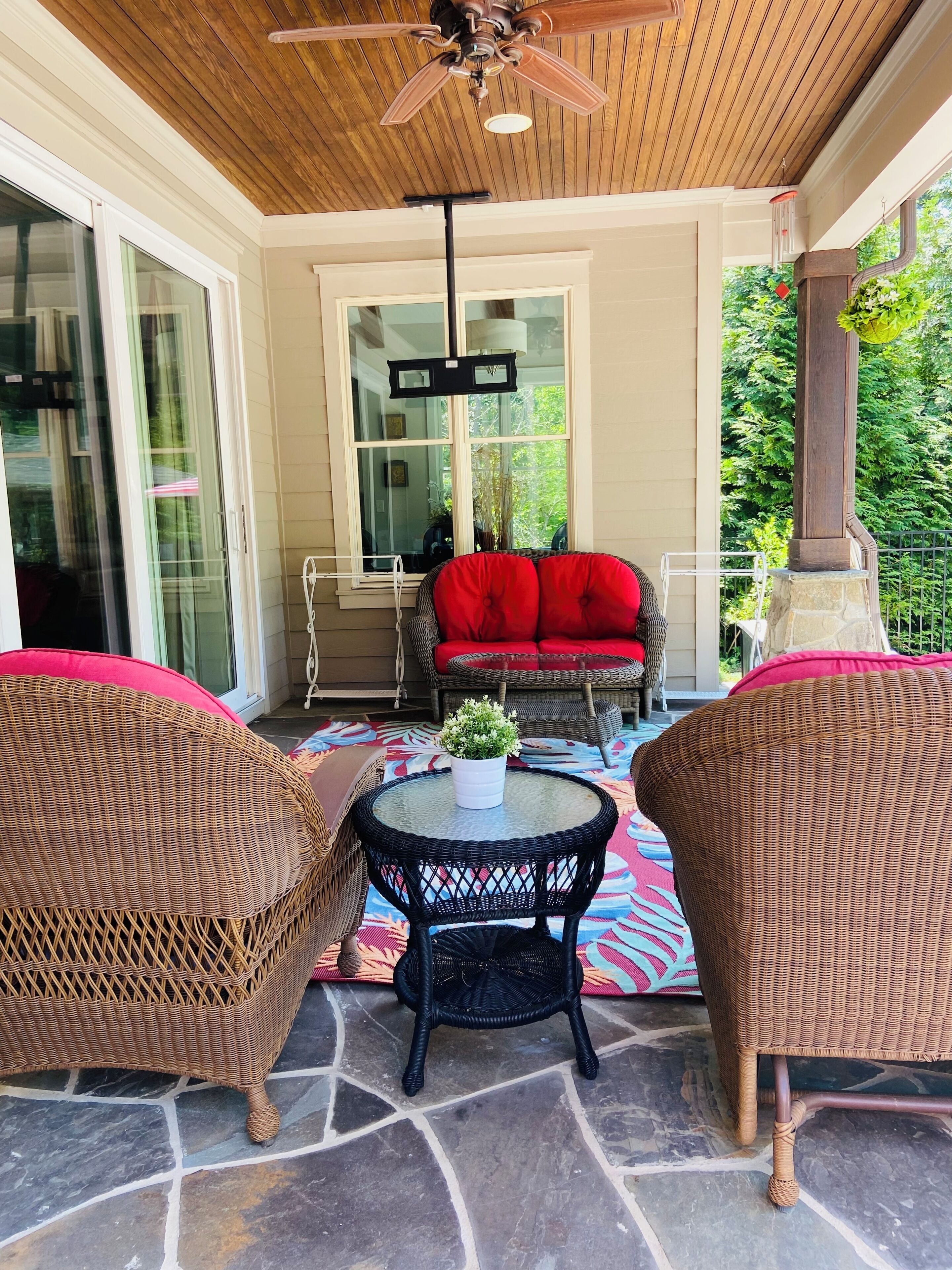 A covered patio with wicker furniture, a stone floor, and a ceiling fan.