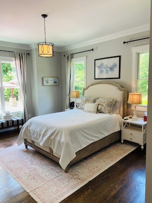 A bedroom with a large bed, bedside lamps, a rug, and a window with curtains.