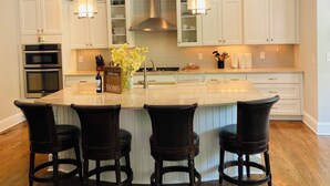 Una cocina moderna con armarios blancos, una isla central con taburetes de bar, electrodomésticos de acero inoxidable e iluminación colgante.