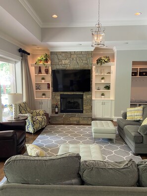 A living room with a stone fireplace, a flat-screen TV, and a chandelier.