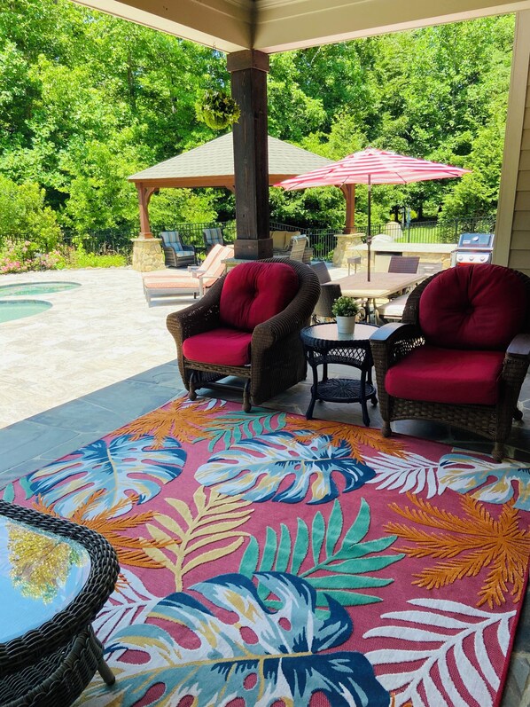 A covered patio area with wicker furniture, a pool, and a colorful rug.