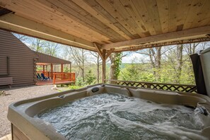 Un bain à remous sous une pergola en bois, avec vue sur une terrasse en bois et des arbres.