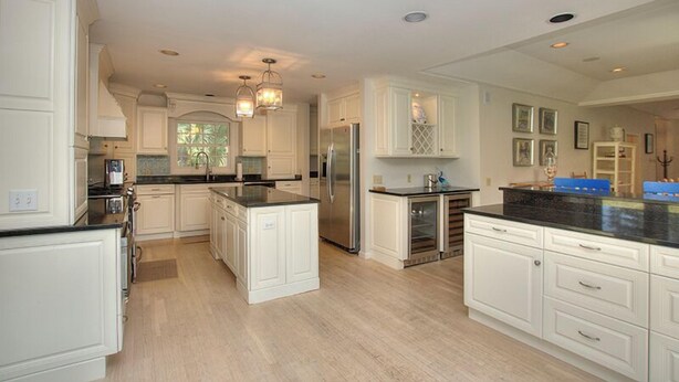 A spacious kitchen with white cabinetry, a central island, and a stainless steel refrigerator.