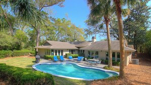 A house with a swimming pool, surrounded by palm trees and a well-maintained lawn.