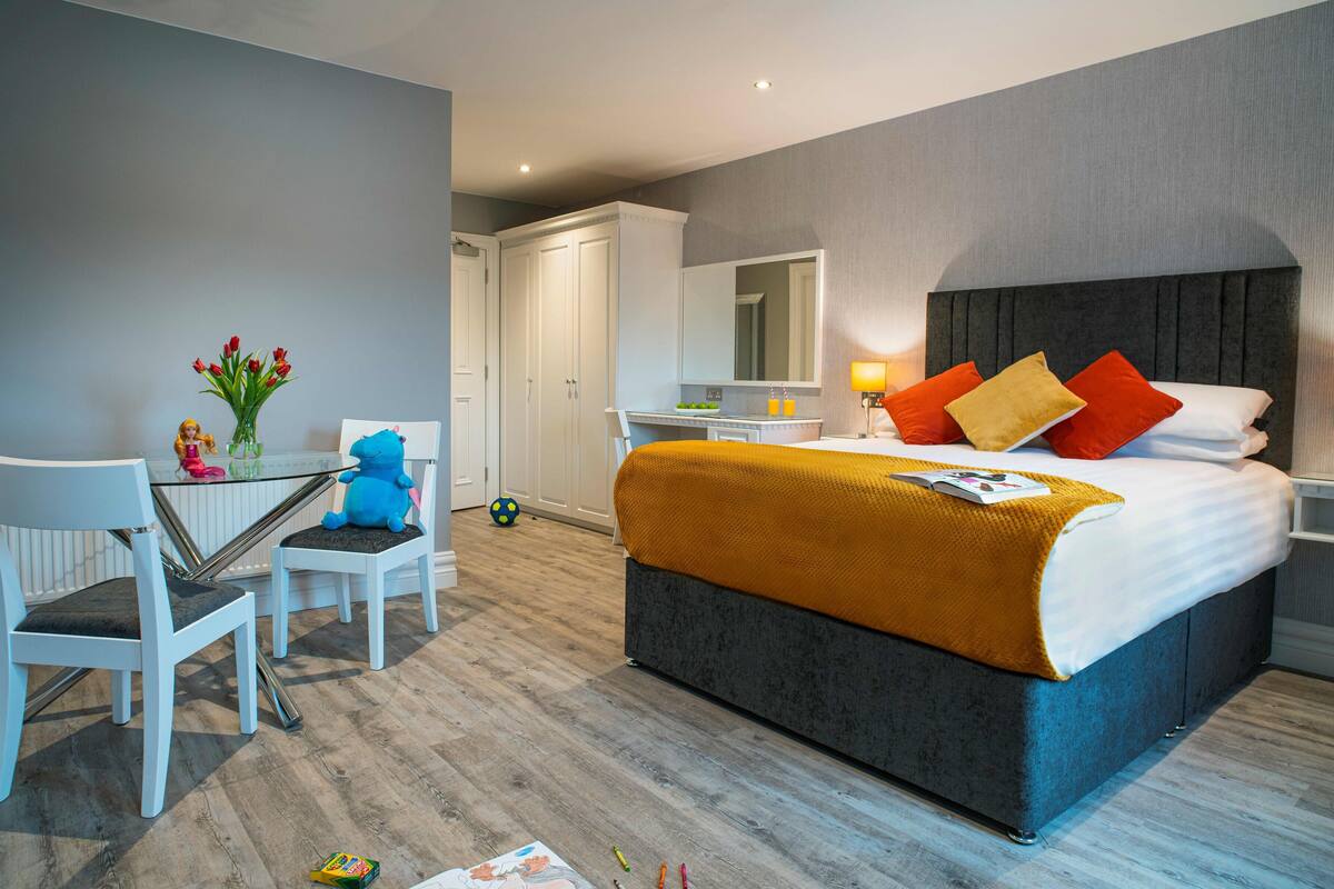 Una habitación de hotel moderna con una cama grande, un escritorio, una silla y una mesita con un florero.