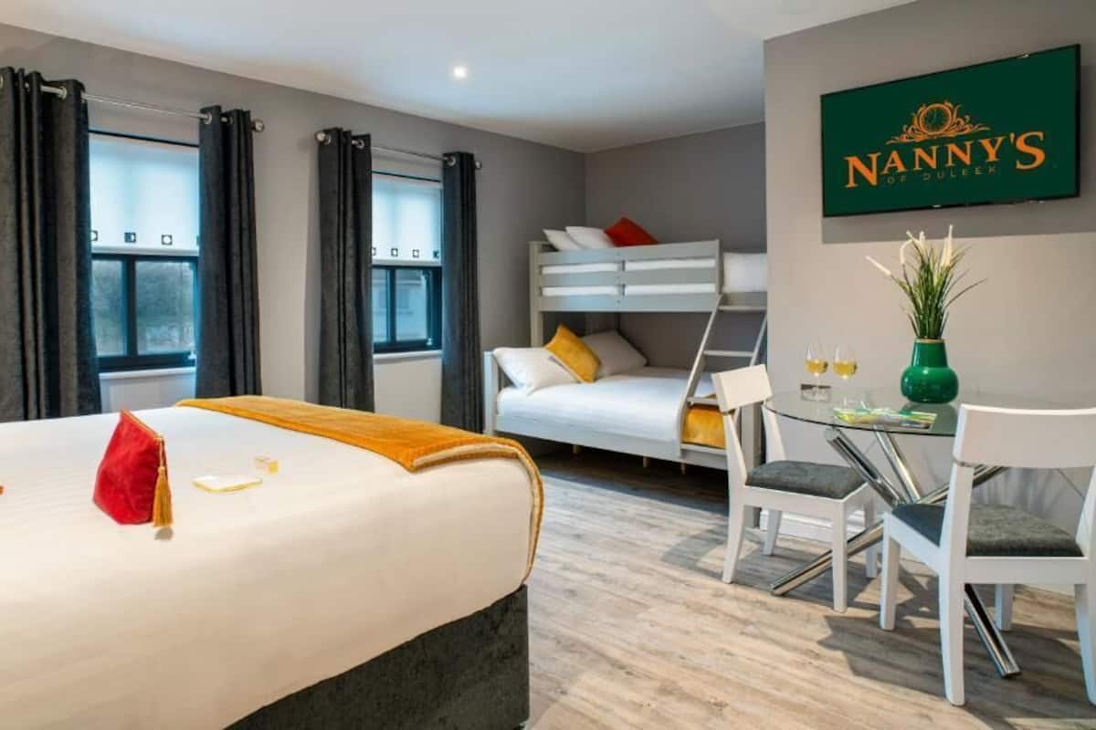 Una habitación de hotel con una cama litera, un escritorio con dos sillas, un florero con flores y un cartel enmarcado en la pared.