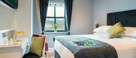 Ein Hotelzimmer mit einem Bett, einem Schreibtisch mit Stuhl, einem Fenster mit Vorhängen und Blick nach draußen.