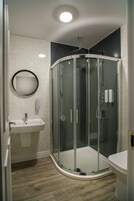 Un baño moderno con ducha envuelta en vidrio, un lavabo blanco y un inodoro.