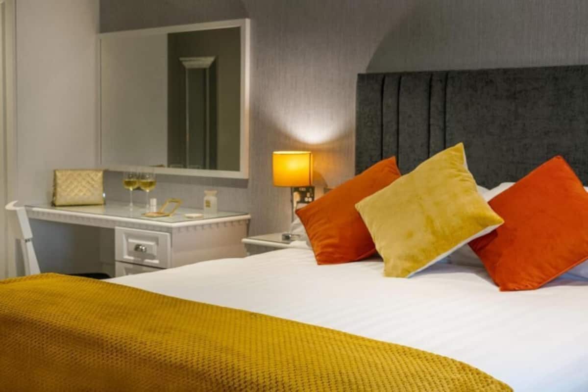 Una habitación de hotel con cama, escritorio, espejo y lámpara.