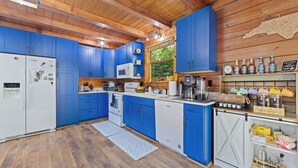 Une cuisine avec des meubles de couleur bleue, un réfrigérateur blanc, un four à micro-ondes, un coin café et un plafond en bois.