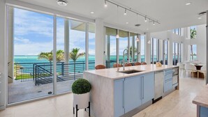 A modern kitchen with a large island, large windows, and a view of the ocean. - Siesta Sunset Sanctuary: Incredible Sunset Views! (Siesta Key)
