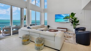 A spacious living room with a large white sofa, a coffee table, and a view of the ocean through large windows. - Siesta Sunset Sanctuary: Incredible Sunset Views! (Siesta Key)