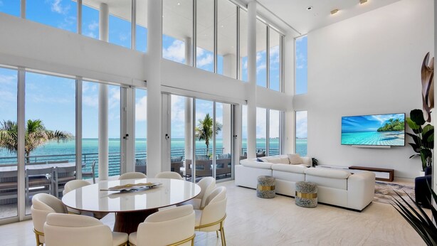 A spacious room with a large round table and chairs, a white sofa, and a television on the wall. - Siesta Sunset Sanctuary: Incredible Sunset Views! (Siesta Key)