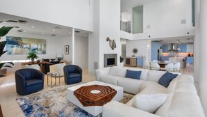 A spacious living area with a white sofa, blue armchairs, and a coffee table. A kitchen is visible in the background. - Siesta Sunset Sanctuary: Incredible Sunset Views! (Siesta Key)