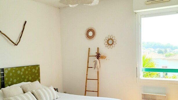 A bedroom with a bed, a ladder, a ceiling fan, and a window with a view. - Cosy mountain view apartment, 2 bedrooms, terrace and parking box (Hendaye)