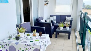 A balcony with a dining table, chairs, and potted plants. There is a sofa and a small table with a decorative item. - Cosy mountain view apartment, 2 bedrooms, terrace and parking box (Hendaye)