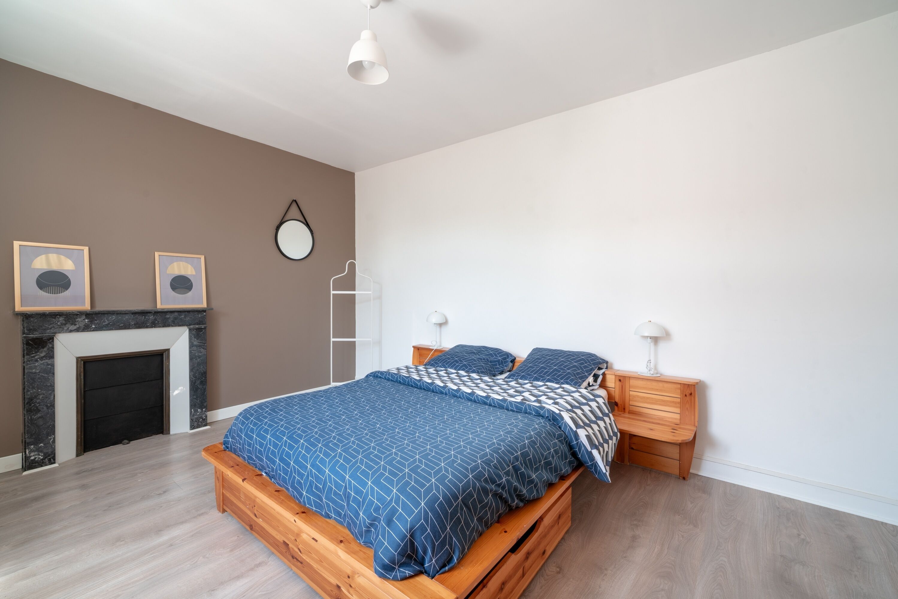 Ein Schlafzimmer mit einem Bett, Nachttischen aus Holz, einem Kamin und Wandleuchten.