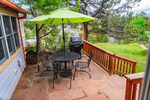 A patio with a round table and chairs, a green umbrella, and a barbecue grill. - Vintage Cabin w/ Views in Heart of Estes (Estes Park)