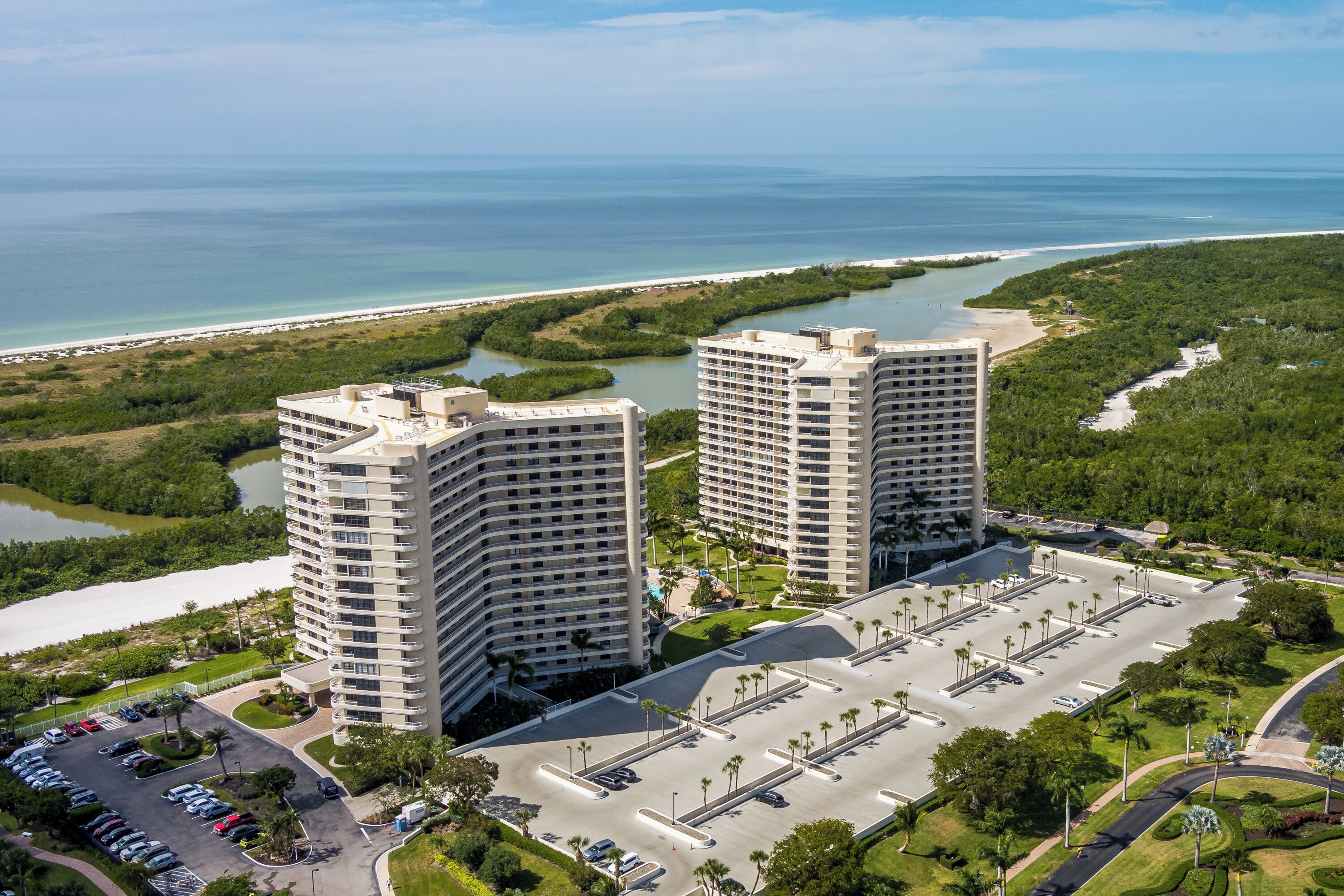 Ein Hochhaus-Hotel mit Parkplatz, umgeben von Grünflächen und Blick auf den Strand.
