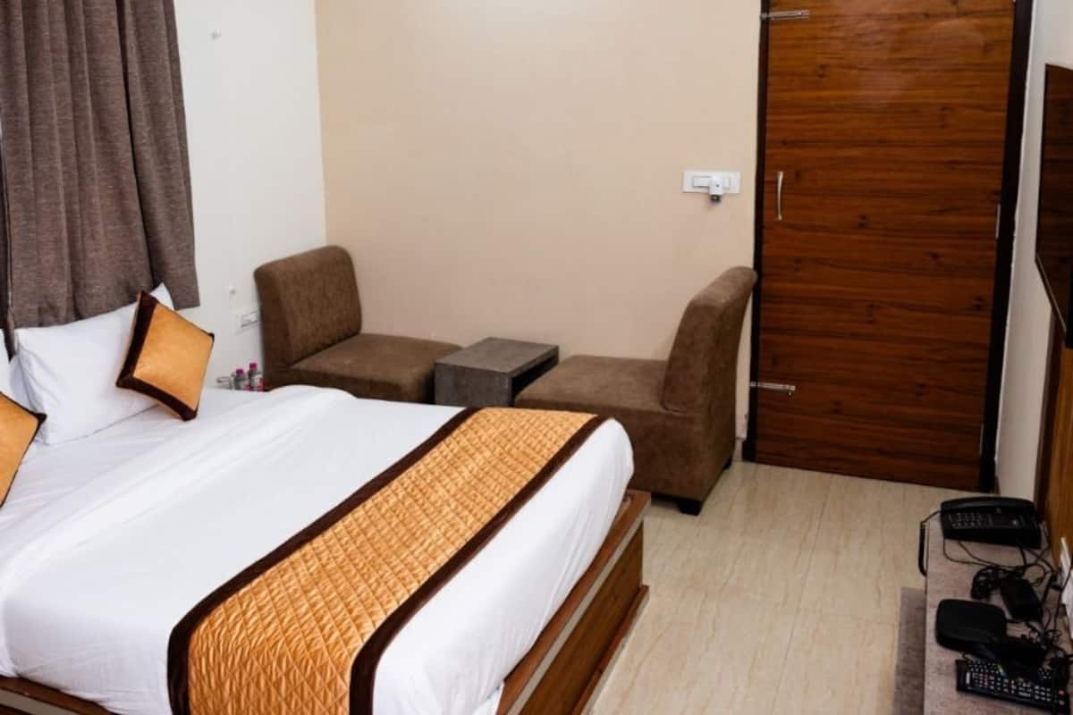 A hotel room with a bed, two chairs, a small table, a TV, and a wooden door.