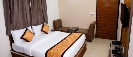 Habitación de hotel con una cama, dos sillas, una mesita, un televisor y una puerta de madera.
