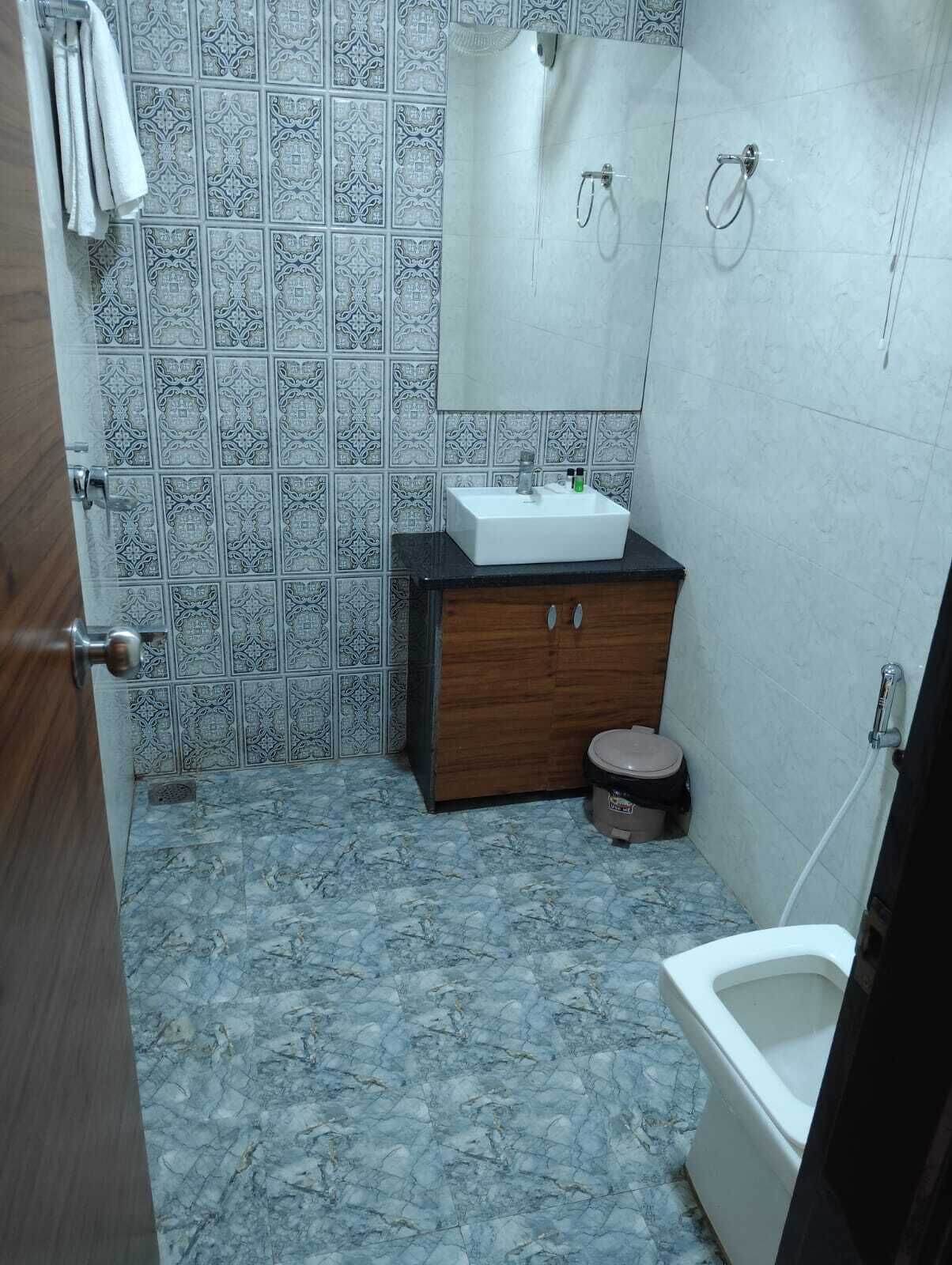 Un baño con lavamanos, inodoro y ducha. Las paredes tienen azulejos estampados, y hay un gabinete de madera con un espejo sobre el lavamanos.