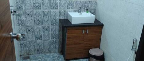 Un baño con lavamanos, inodoro y ducha. Las paredes tienen azulejos estampados, y hay un gabinete de madera con un espejo sobre el lavamanos.
