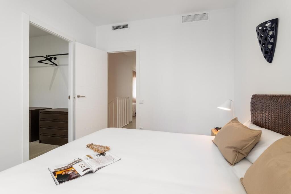 A modern bedroom with a bed, a bedside table with a lamp, a magazine on the bed, and a wardrobe with a hanging rack.