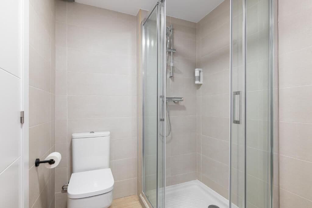 Een moderne badkamer met een douchecabine van glas, een toilet en een handdroger.