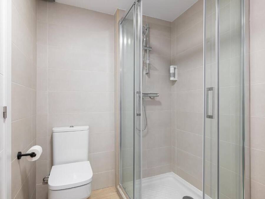 Een moderne badkamer met een douchecabine van glas, een toilet en een handdroger.
