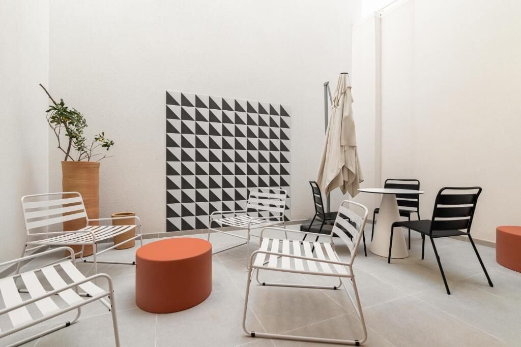 Un café moderno y minimalista con sillas y mesas de estructura metálica, un pared con diseño geométrico y una planta en maceta.