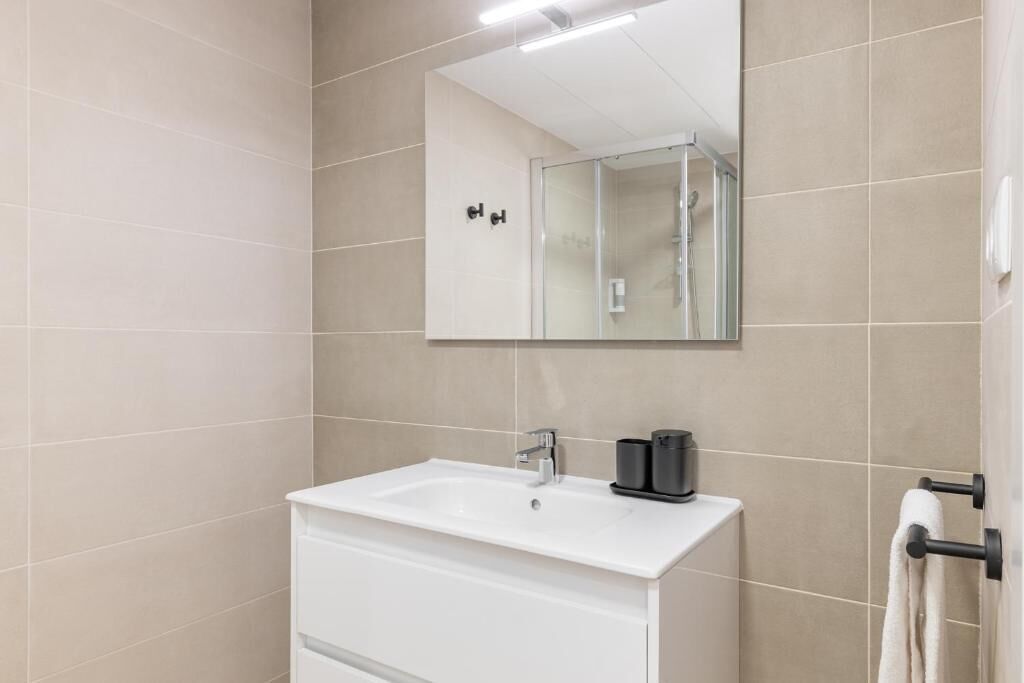 Une salle de bain moderne avec un lavabo blanc, un miroir et une douche à parois de verre.