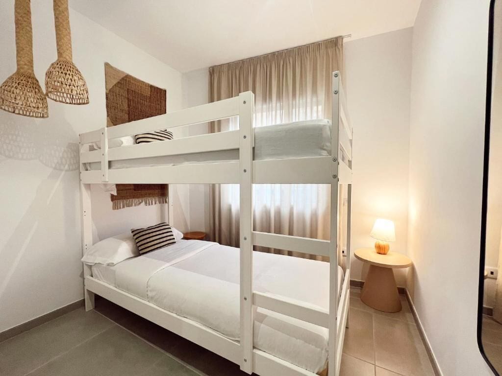 Habitación con literas, una mesita de noche con lámpara, un tapiz de pared tejido y una ventana con cortinas.