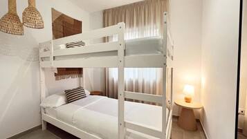 Habitación con literas, una mesita de noche con lámpara, un tapiz de pared tejido y una ventana con cortinas.