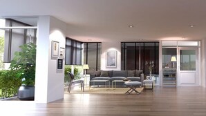 A spacious living room with a sofa, a coffee table, and a dining area with a table and chairs. There is a large window with blinds, a plant, and artwork on the walls. - Plume Residence Minburi (Bangkok)