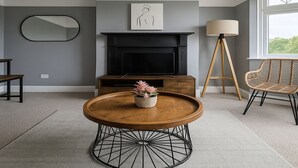 A living room with a fireplace, a round coffee table, a wicker chair, and a floor lamp. - Beautiful 1 bed flat in Wimbledon (London)