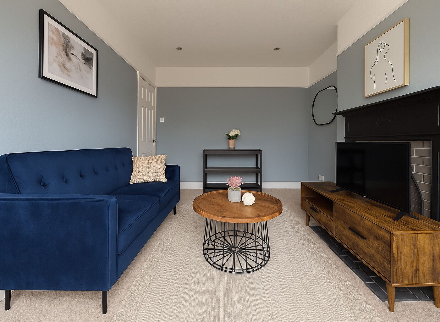 A modern living room with a blue sofa, a round wooden coffee table, a TV, and a fireplace.