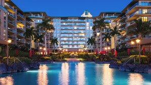 A multi-story hotel with a swimming pool surrounded by palm trees and red umbrellas.