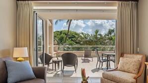 A hotel room with a balcony, a sofa, a chair, a table, and a lamp.